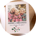 Two children in festive Christmas outfits laugh in front of a decorated tree