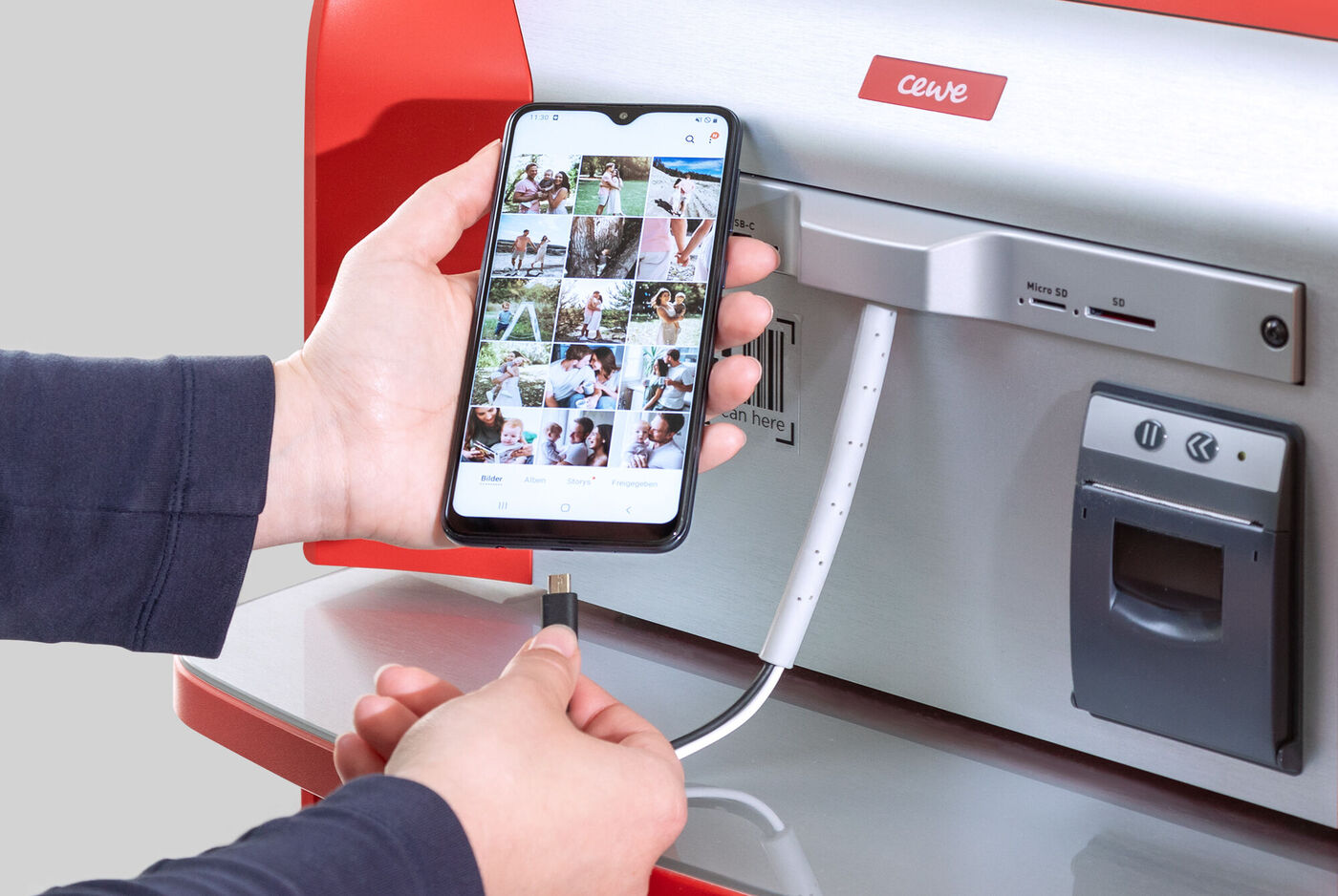 Person connects a smartphone to a CEWE photo kiosk for photo selection.