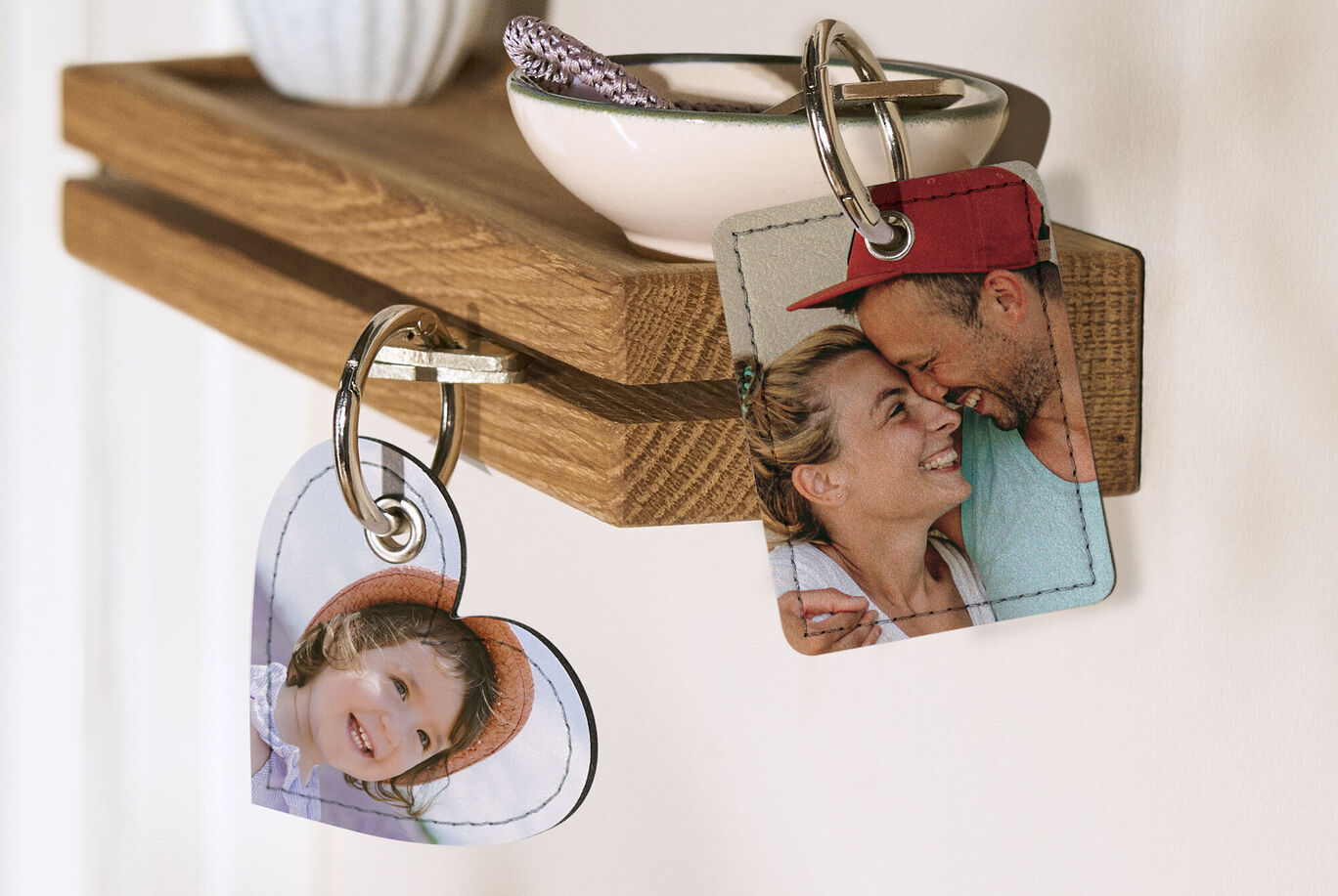 Two personalized keychains hanging on a wooden shelf. The heart keychain features a picture of a person, and the right one shows a couple. Beautiful keepsakes for loved ones.